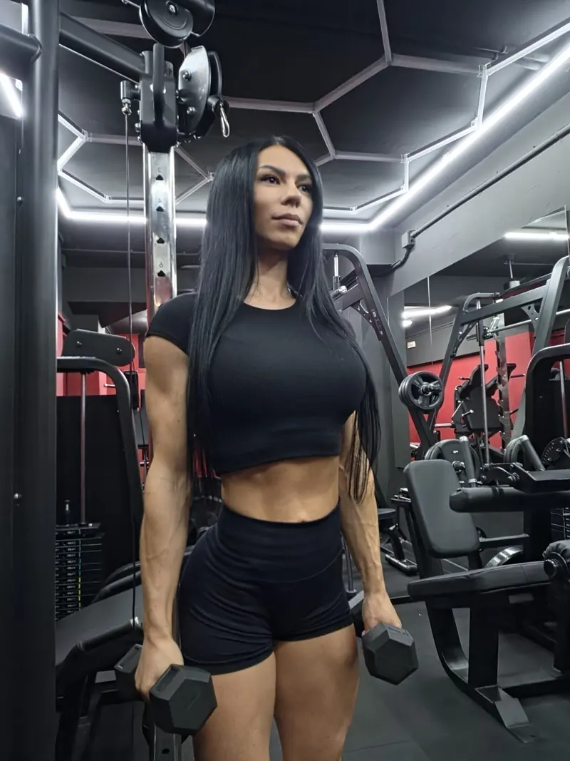 Natasha, de pie con una mancuerna en cada mano, con top y shorts negros en la sala de entrenamiento del local de Gràcia, con techo de luces hexagonales y paredes rojas